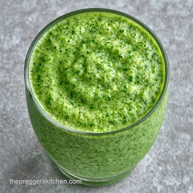 Vibrant green smoothie in a tall glass with a reusable straw, set against a bright white background with mint leaves.