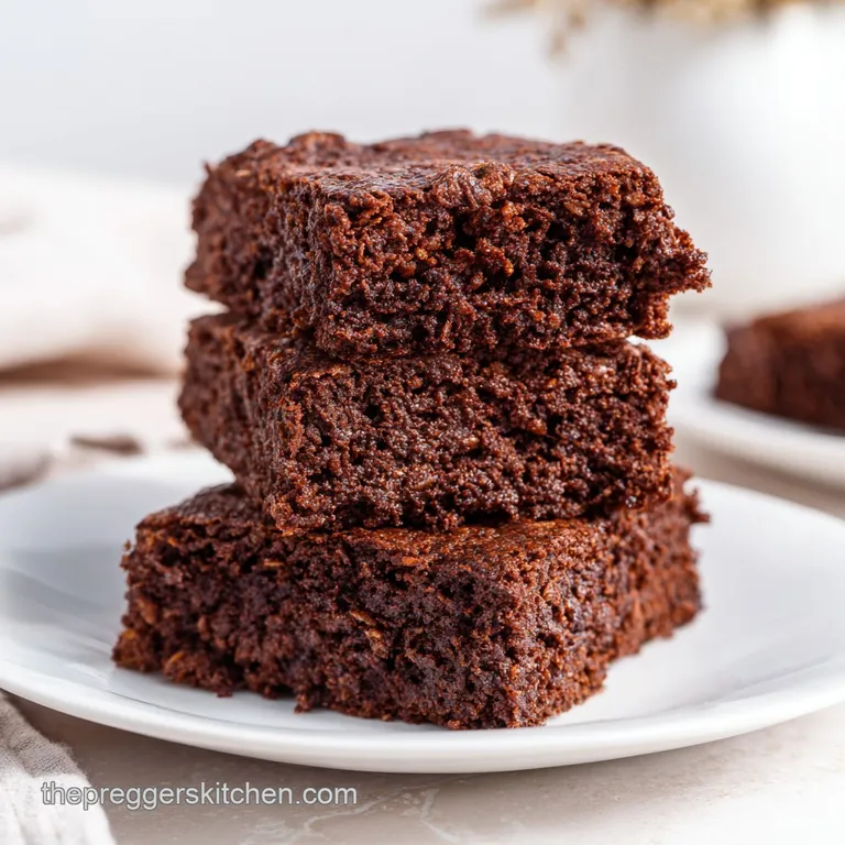 A neat stack of dark chocolate squares on a white ceramic plate, dusted with cocoa powder and a mint leaf garnish.