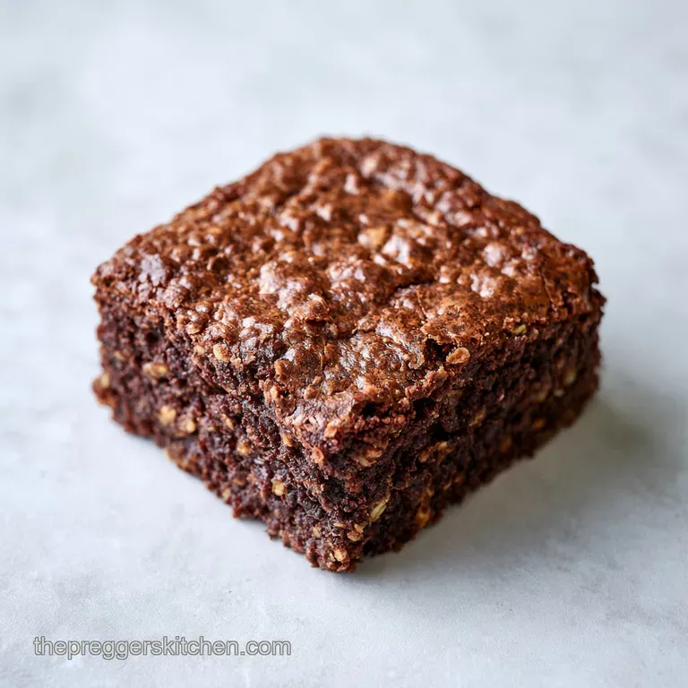 Single square of fudgy chocolate brownie on a white ceramic plate, accented by a swirl of cream and a mint leaf.
